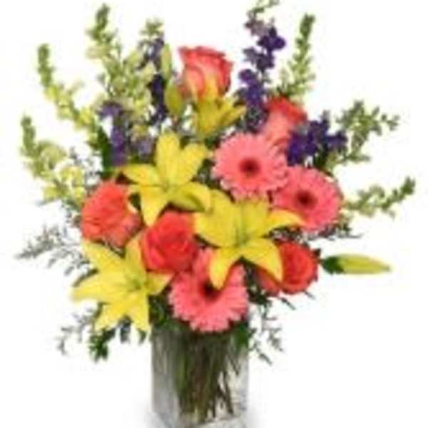 Mixed bouquet with lilies, gerbera daisies, roses, and purple accents in a glass vase