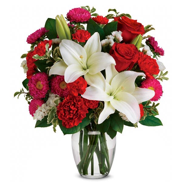 Bouquet of red and pink flowers with white lilies in a clear glass vase