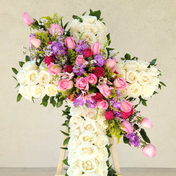 Large cross-shaped floral arrangement of white, pink, and purple roses on an easel