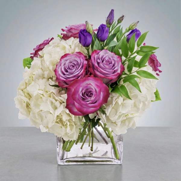Pink and purple roses with white hydrangeas in a clear square vase