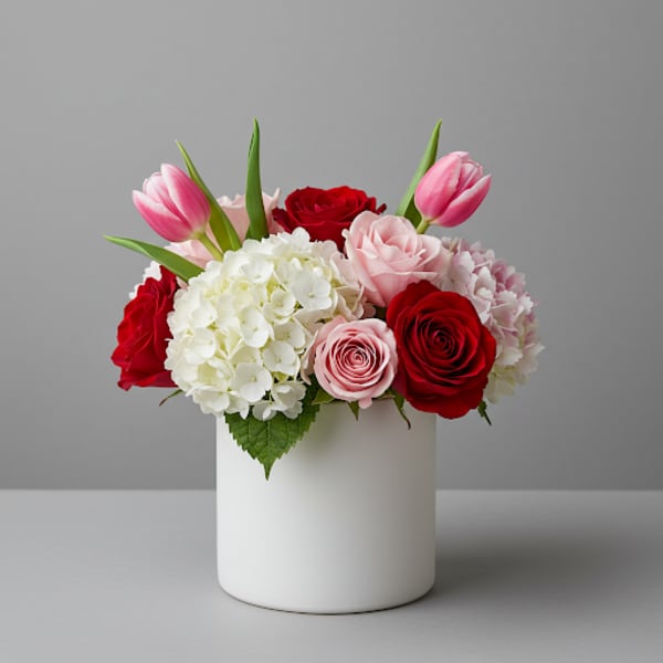Pink tulips, red and blush roses, and white hydrangeas in a white vase