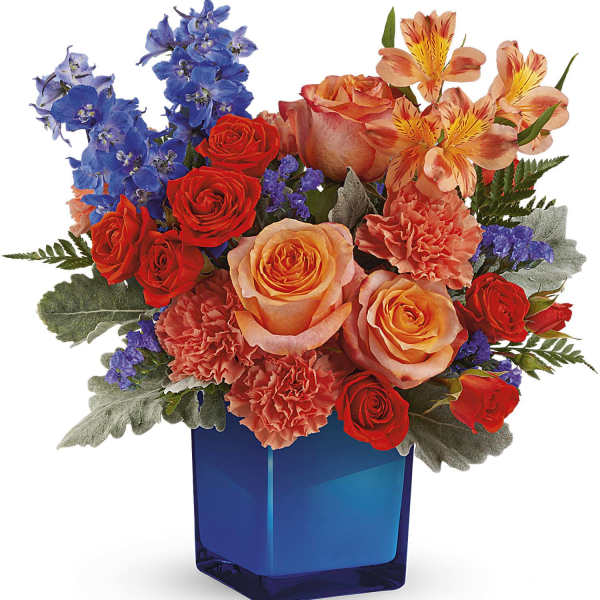 Mixed bouquet of roses, carnations, and blue flowers in a blue vase