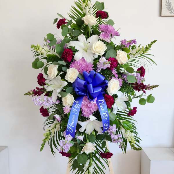 Tall funeral spray with white lilies, roses, and purple flowers on an easel