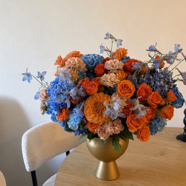 Colorful bouquet of orange, blue, and peach flowers in a gold vase