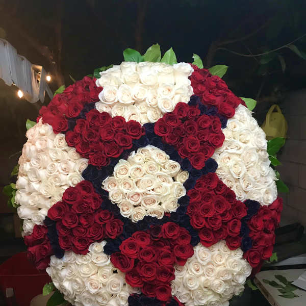 Large circular arrangement of red, white, and dark blue roses on an easel
