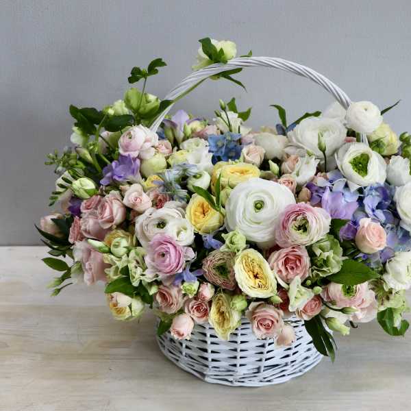 Pastel basket arrangement of white ranunculus, pink roses, and yellow blooms in a white wicker basket