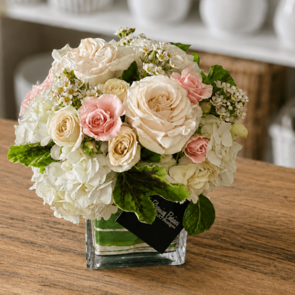 Compact bouquet of cream and pink roses in a clear square vase