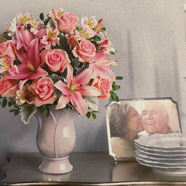 Pink roses and lilies arranged in a pale vase on a table