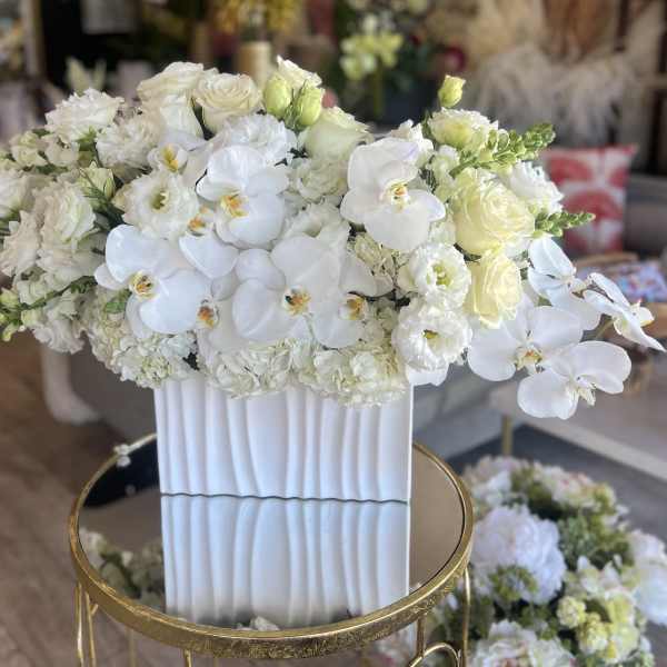White floral arrangement in a tall ribbed vase with orchids and roses