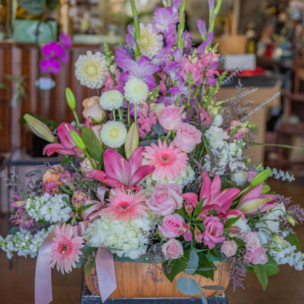 Large pastel flower arrangement with pink lilies, roses, and gerbera daisies in a wooden basket