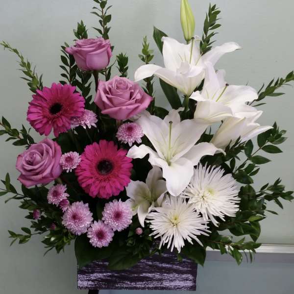 Pink roses and white lilies arranged in a purple container
