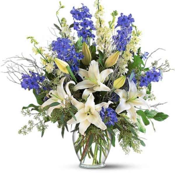 White lilies and blue flowers in a clear glass vase