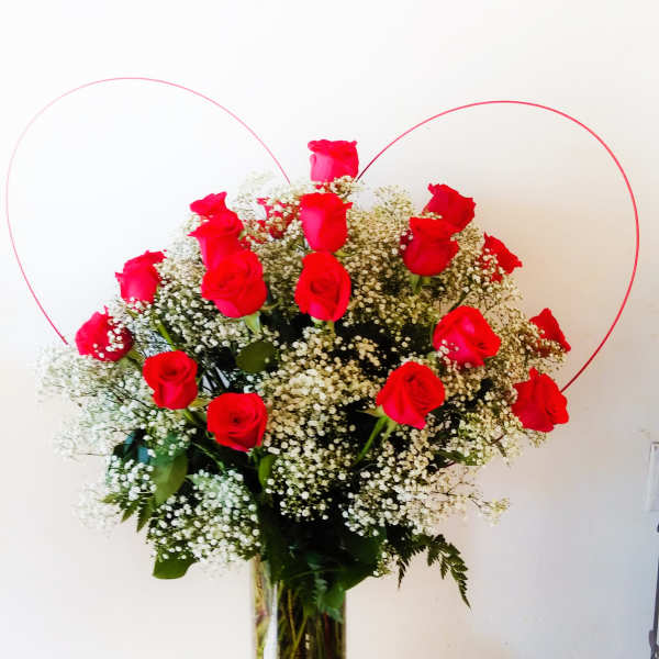 Red roses arranged in a glass vase with baby's breath and heart-shaped wire accents.