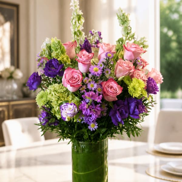 Mixed pink and purple flower arrangement in a tall glass vase
