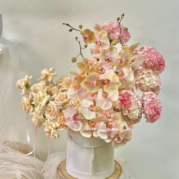 Peach orchids and pink hydrangeas arranged in a white hatbox