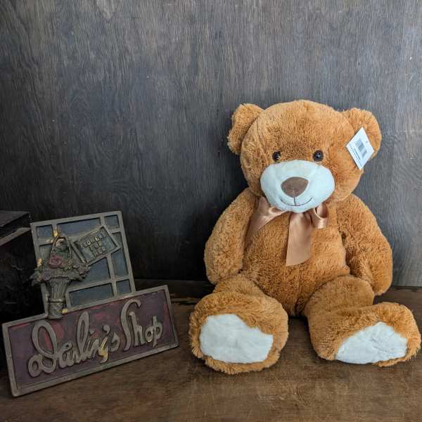 Brown teddy bear with a ribbon sitting beside a glass candle holder
