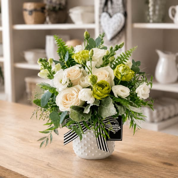 White and pale peach roses in a white textured vase with a striped ribbon