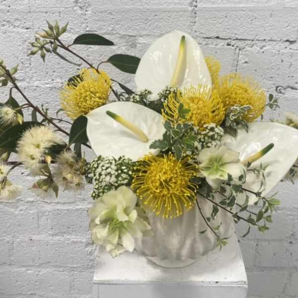 White anthuriums and yellow pincushion blooms in a white vase