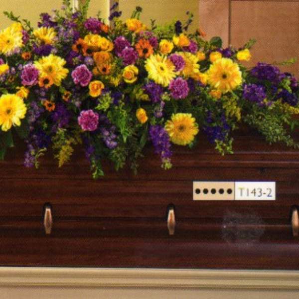 Large floral spray on a wooden casket with yellow and purple flowers