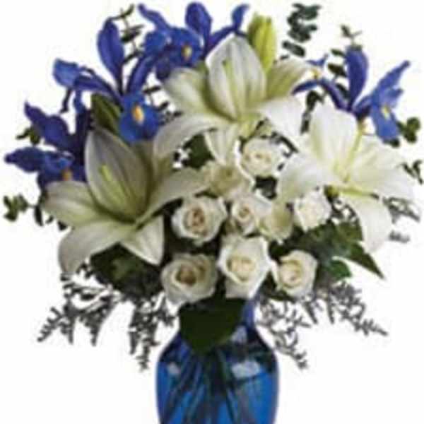 Tall arrangement of white lilies and roses with blue irises in a cobalt glass vase