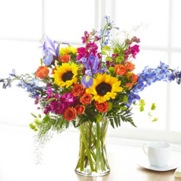 Mixed bouquet with sunflowers, roses, and blue flowers in a glass vase