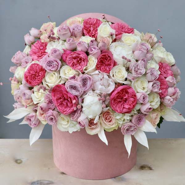 Dense arrangement of pink and white roses and peonies in a round pink hatbox container