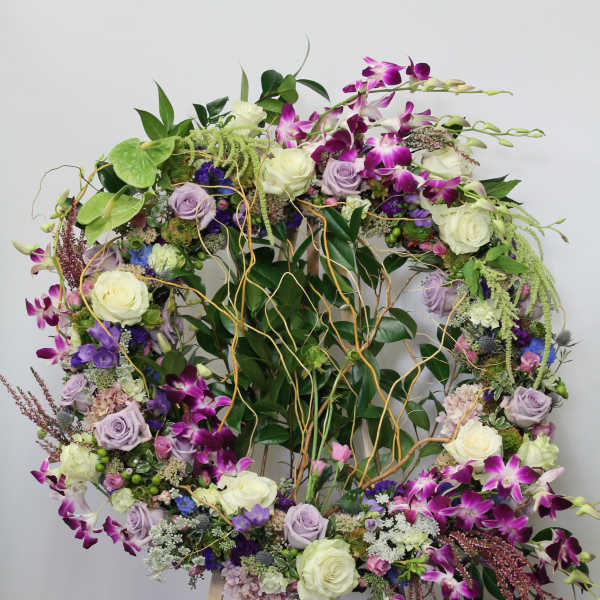 Large floral wreath on an easel with purple orchids and white roses