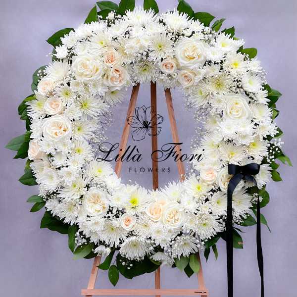 White floral wreath on an easel with a black ribbon