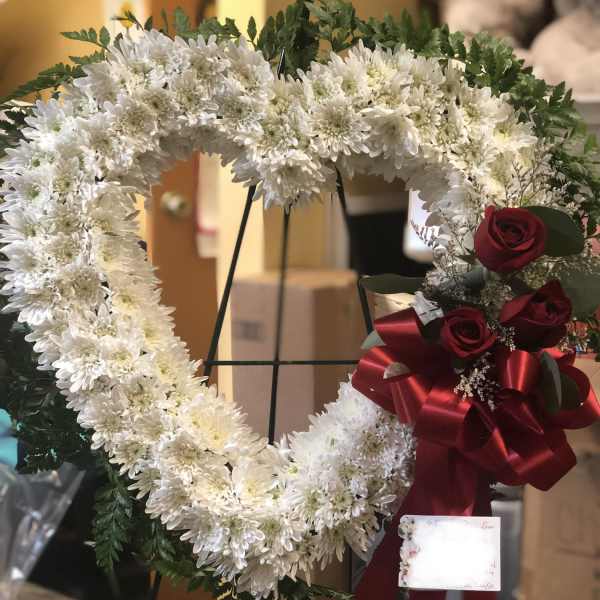 Heart-shaped white chrysanthemum wreath with red roses and a red ribbon
