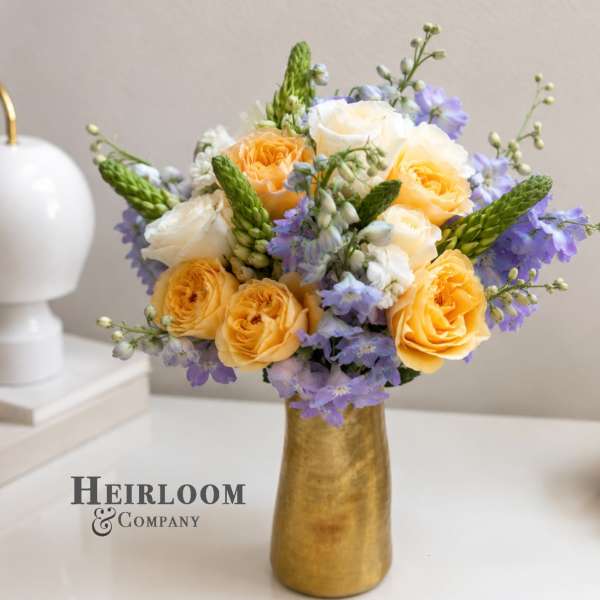 Yellow and white roses with lavender flowers in a gold vase