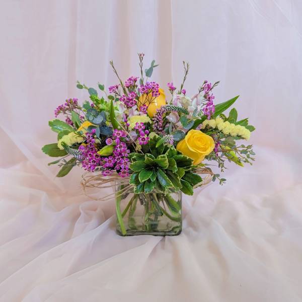 Bouquet of yellow roses and pink filler flowers in a square glass vase