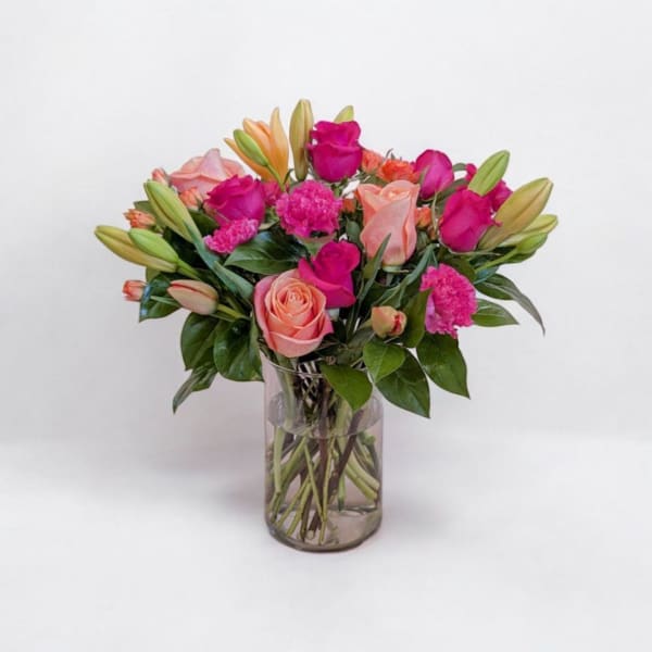Pink and peach roses with lilies and carnations in a glass vase