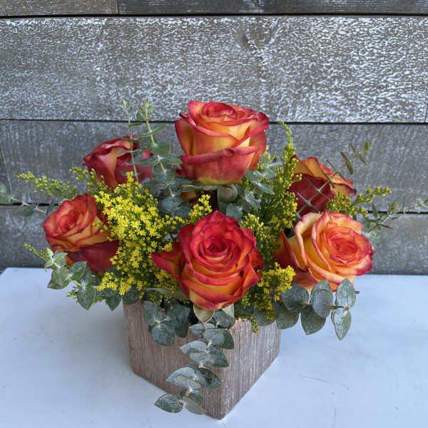 Orange-red roses in a square vase with yellow filler flowers