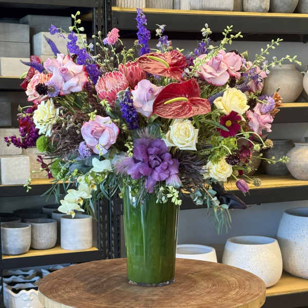Large mixed bouquet in a tall green vase with pink, purple, red, and yellow blooms