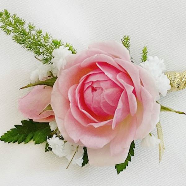 Pink rose boutonniere with white accents and green foliage