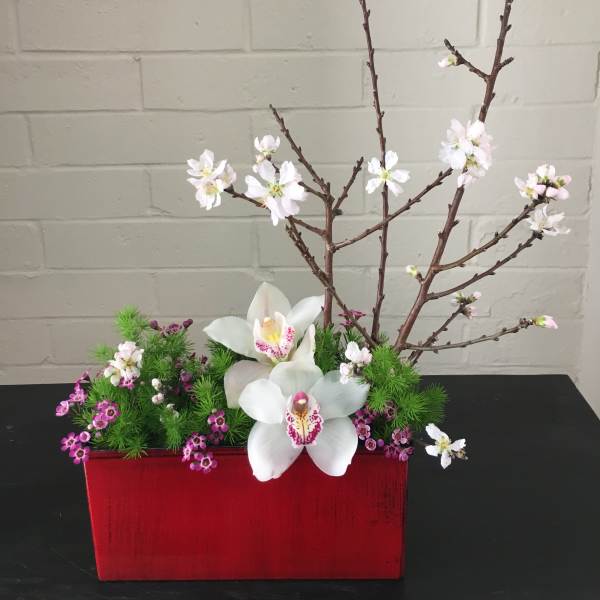 White orchids and pink blossoms in a red rectangular container