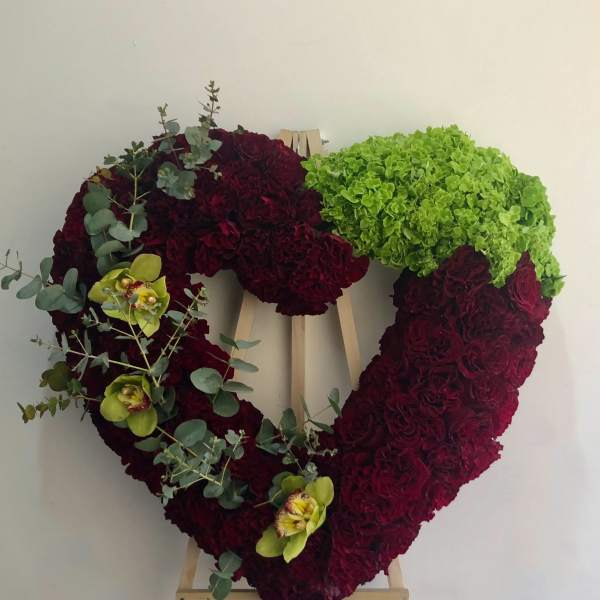 Heart-shaped floral wreath on an easel with burgundy and green blooms