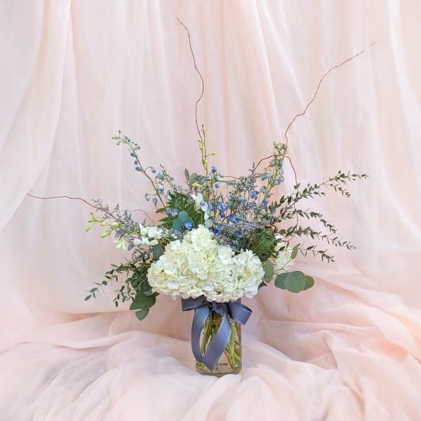 White hydrangea bouquet in a glass vase with blue accents and ribbon