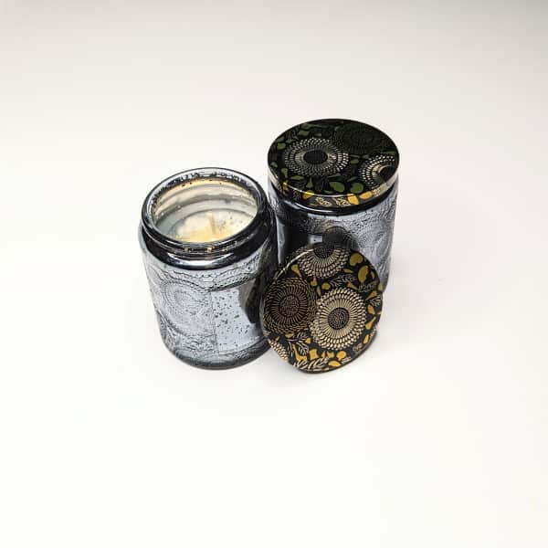 Two decorative candles in patterned glass jars with lids