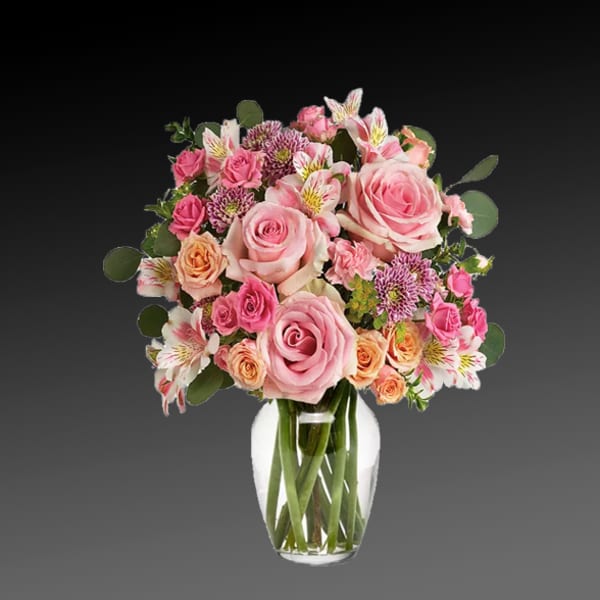 Pink roses and mixed blooms arranged in a clear glass vase