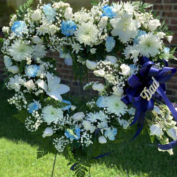 Heart-shaped white floral wreath with blue accents and a purple ribbon