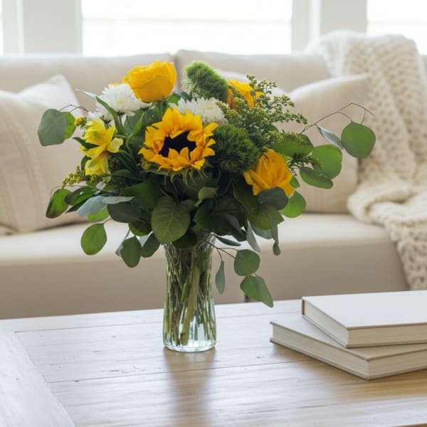 Yellow and white flowers in a clear glass vase on a coffee table