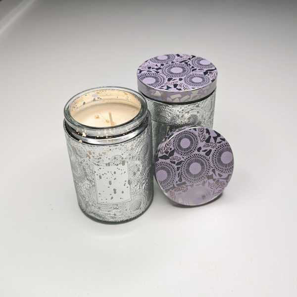 Two glass jar candles with patterned lids on a white surface