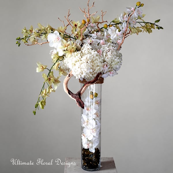 Tall floral arrangement with white orchids and pale blossoms in a glass vase