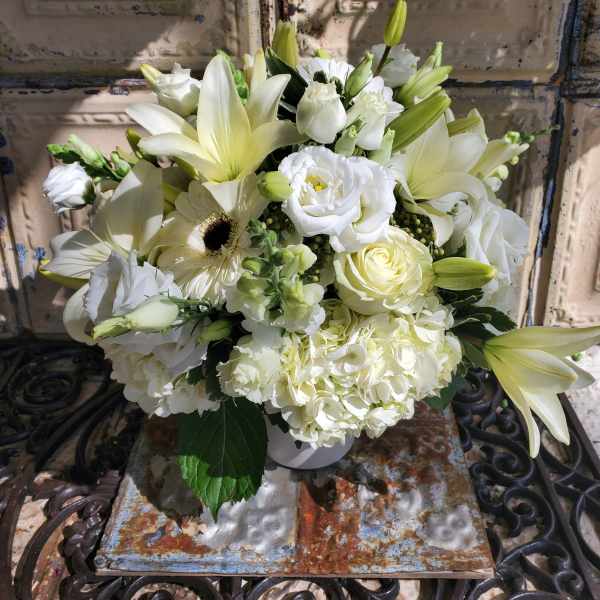 White floral arrangement with lilies, roses, hydrangeas, and a gerbera daisy in a vase