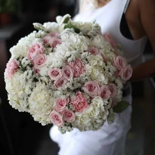 Woman holding a large bouquet of pink and white roses and hydrangeas