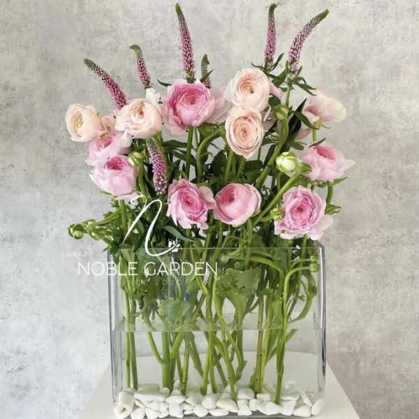 Pink ranunculus and pale roses in a clear rectangular vase