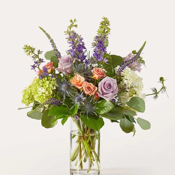 Mixed bouquet of roses, hydrangeas, and purple spikes in a clear glass vase