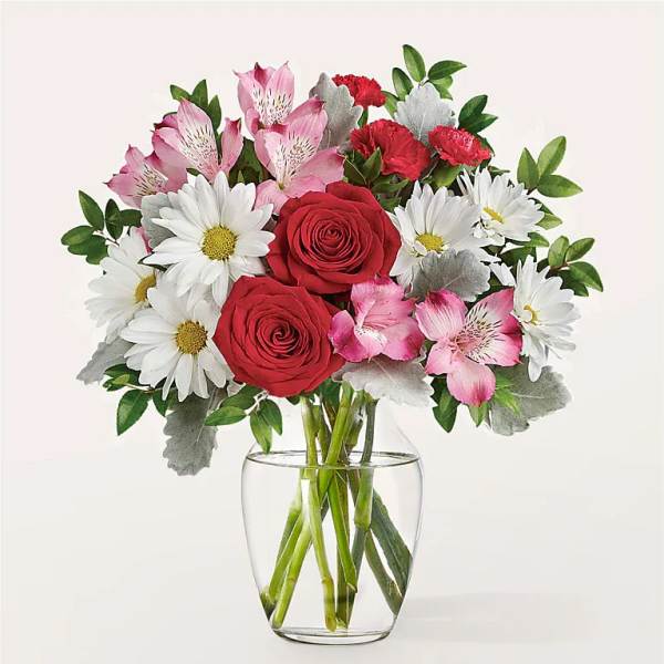 Bouquet of red roses, white daisies, and pink alstroemeria in a clear glass vase
