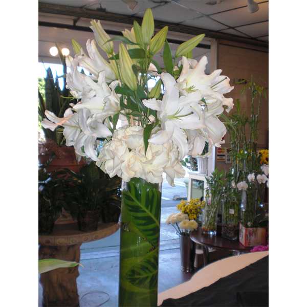 Tall white lily arrangement in a green glass vase